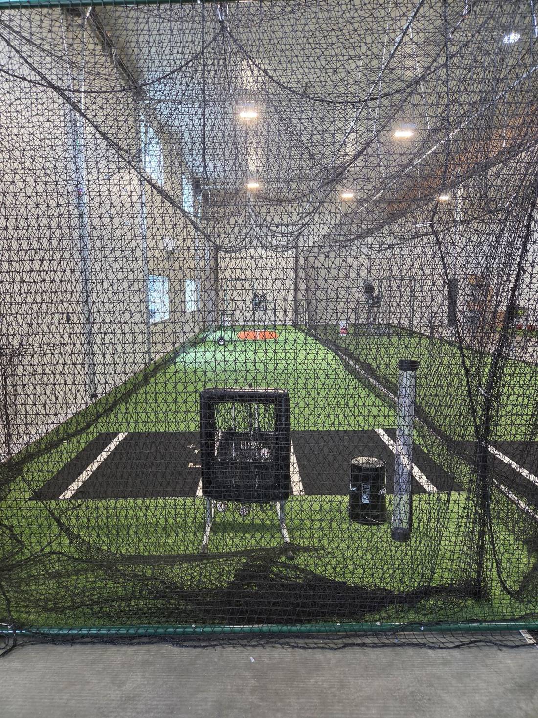 Inside a netted 509 Fun batting cage with green turf, a pitching machine and an L-screen